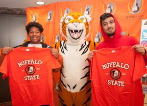 Two smiling students flanking the Benji mascot and holding Buffalo State T-Shirts