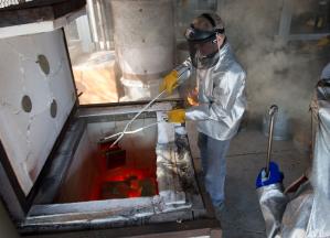 Faculty member in protective clothing lowering ceramic piece into a red-hot kiln with a tongs