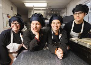Four hospitality students dressed in black chefs uniforms pose for the camera
