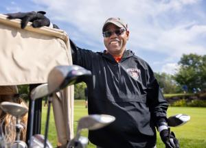 man standing with golf cart and clubs