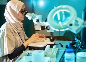 Student wearing hijab looking through lens of microscope