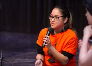 Student in orange Anne Frank T-shirt holding and speaking into microphone