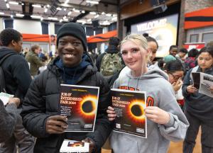 Two students at the CAPE Job Fair holding eclipse flyers and smiling