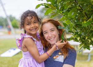 A smiling woman holding a child by a tree