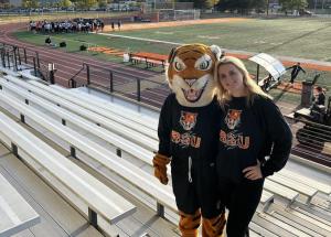 Alumnus and Benji the Bengal standing in the bleachers of Coyer Field