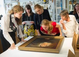 Art conservation professor and visitors closely examining a large framed painting