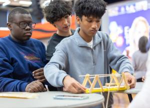 Three male students building a bridge of popsicle sticks