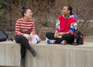 Two students sitting laughing on concrete planter in Student Union Quad