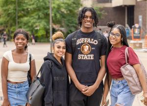 Four smiling students in the Plaza on a sunny day