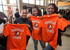 Three smiling students holding upu Buffalo State T-shirts